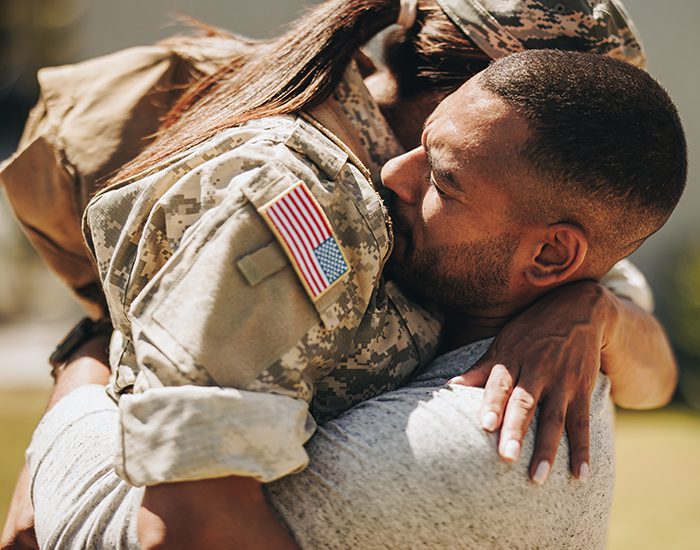 An African American woman wearing combat fatigues and a man in a t-shirt are embracing.