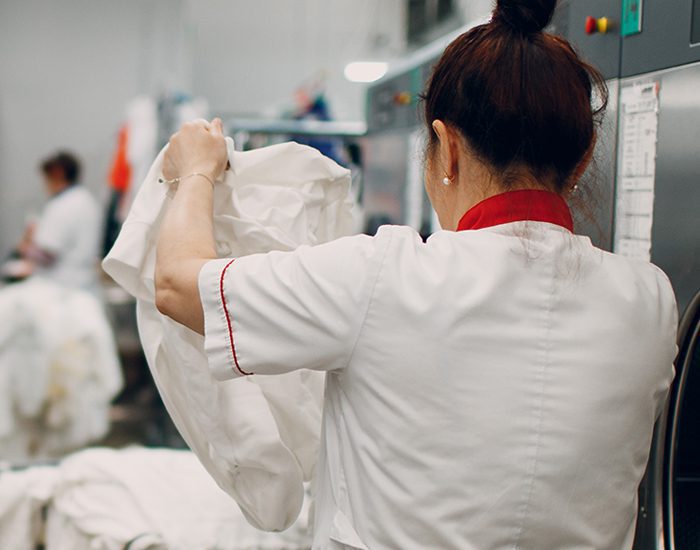 A laundry woman is in in an industrial laundry. Her hair is in a bun on top of her head. She is wearing a uniform and is inspecting sheets for hotels.